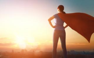 A woman wearing a cape stares off into the sunset