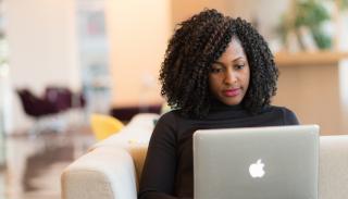 A woman sits on a couch looking at her laptop